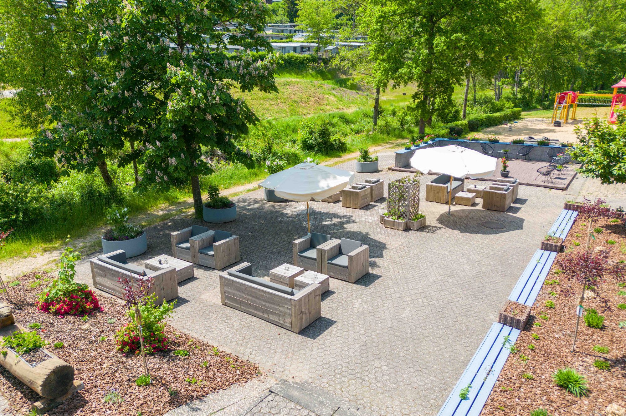 Ferienpark Waxweiler - Eifel Gartenbereich mit Sitzgelegenheiten, Tischen und Spielplatz im Ferienpark